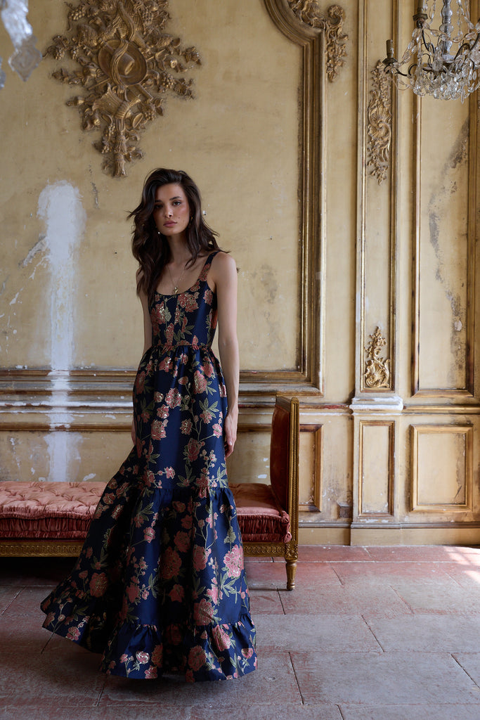 Woman in a floral dress standing in an ornate room with gold walls and a chandelier.