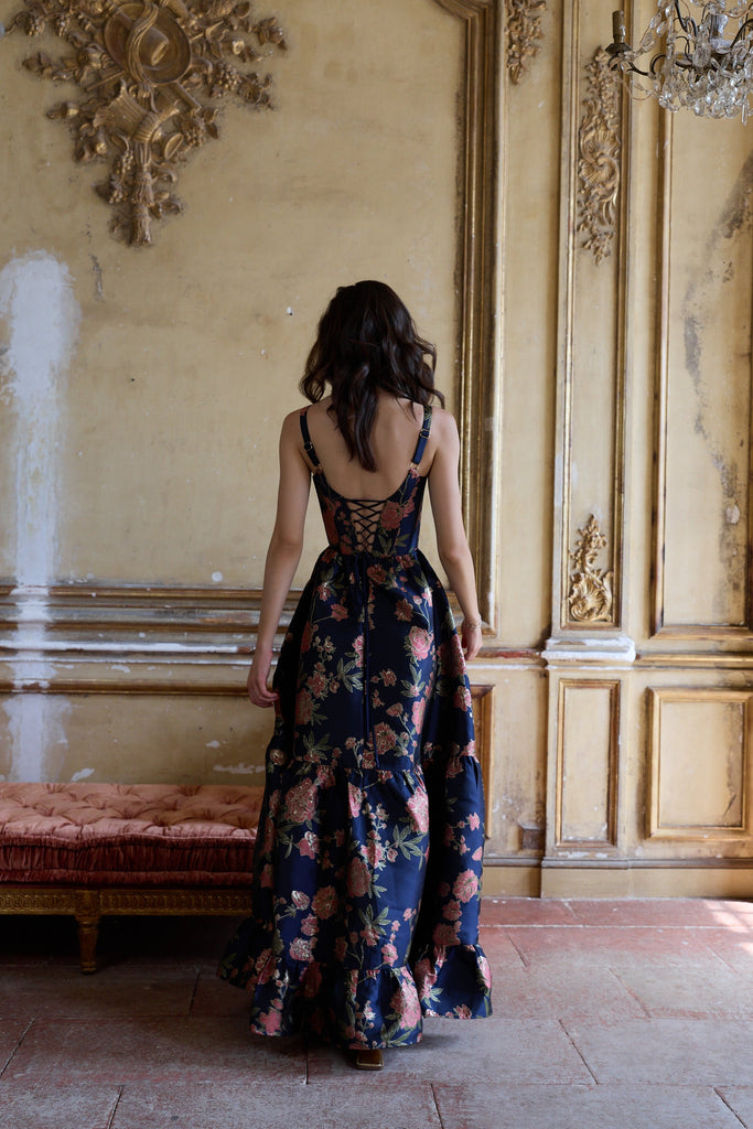 Woman in a floral dress standing in an ornate room with gold walls and a chandelier.