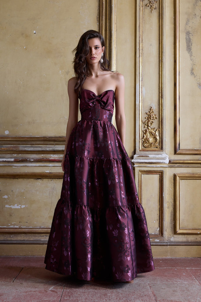 Woman in a burgundy evening gown standing in an ornate room with gold paneling.