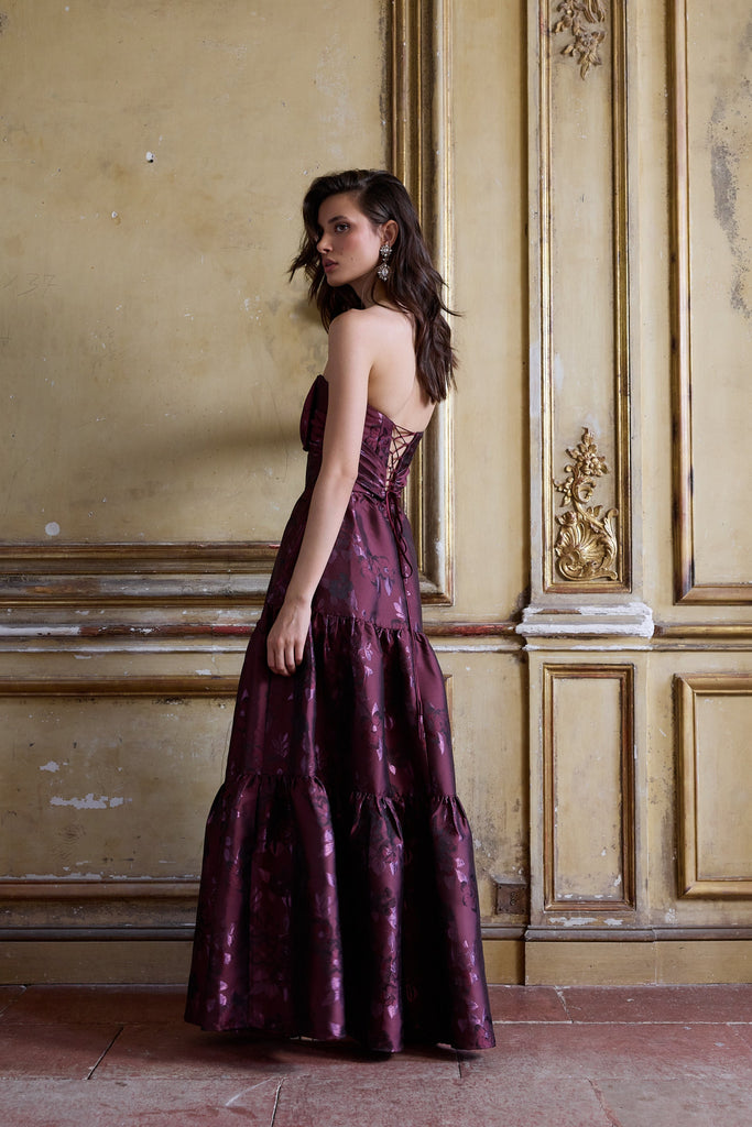 Woman in a purple evening gown standing in an ornate room with gold accents.