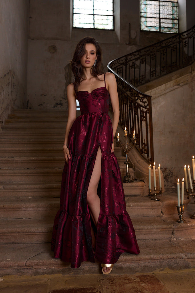 Woman in a burgundy evening gown standing on a staircase with candles.