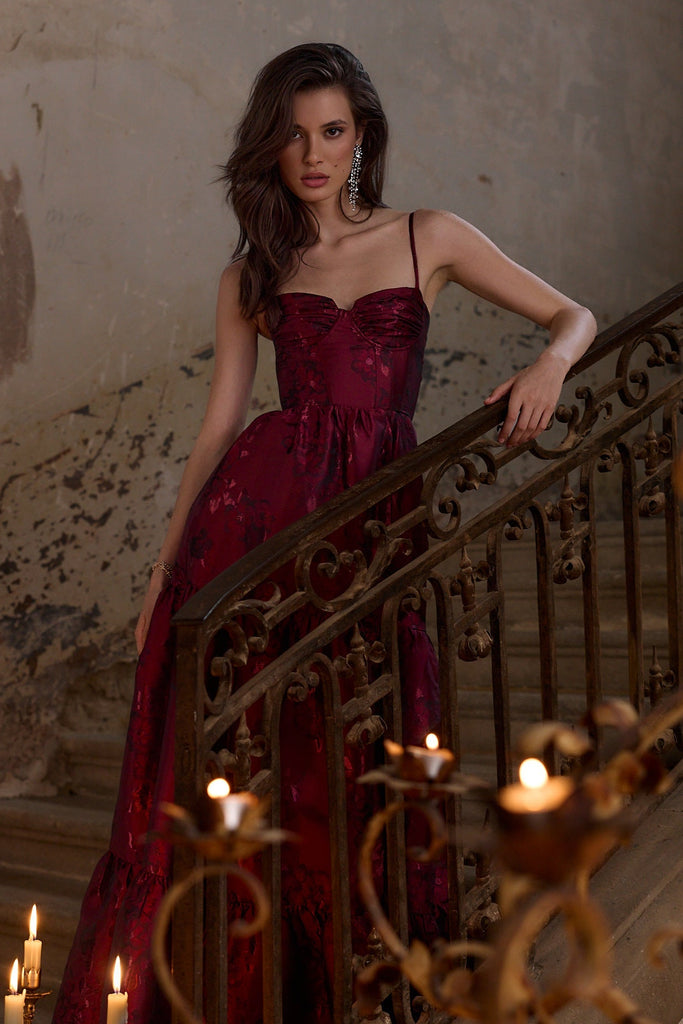 Woman in a red dress standing on a staircase with candles, in a dimly lit room.
