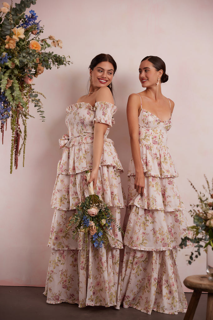 two models wearing dresses in pink rose print. right model showing front and side view wearing angelina dress in pink rose print. right model showing front view wearing caterina dress in pink rose print.