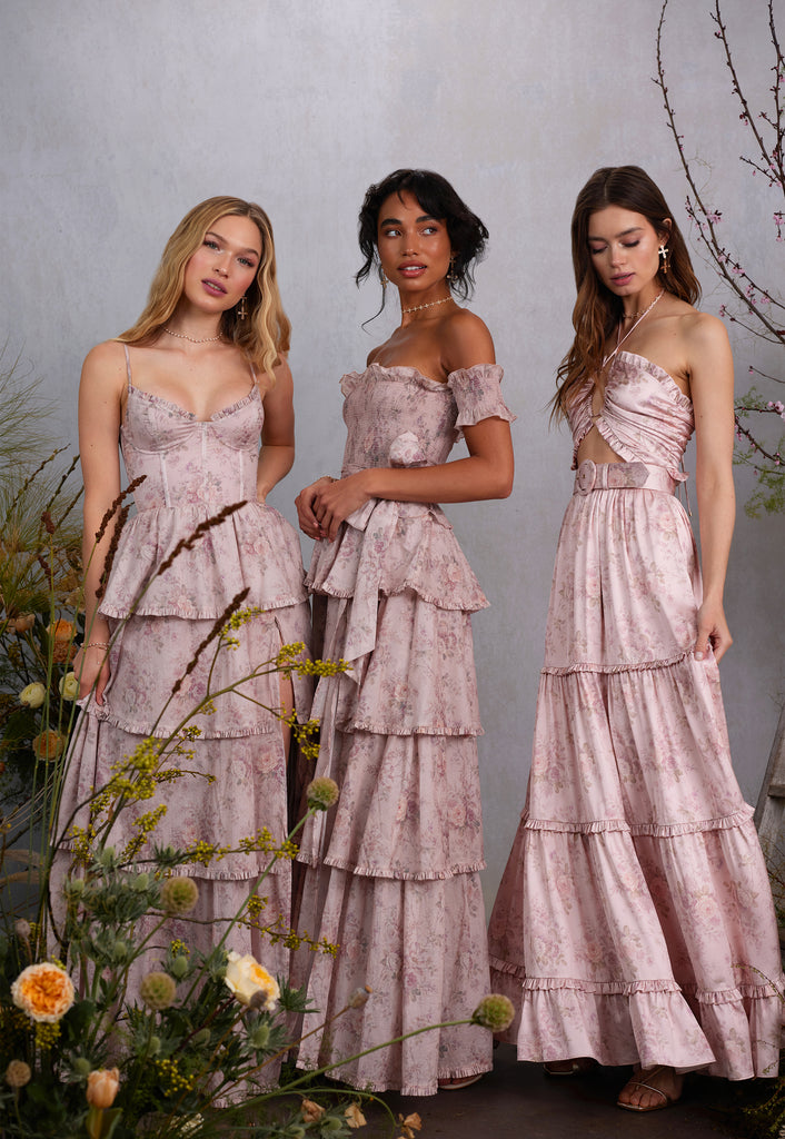three models wearing blush bouquet dresses. left model full front view wearing caterina dress in blush bouquet. middle model full side view of angelina dress in blush bouquet. right model full side view of penelope dress in blush bouquet.