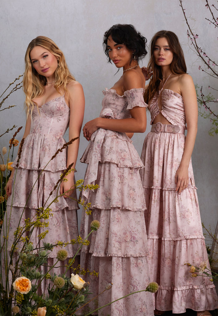 three models wearing blush bouquet dresses. left model front view wearing caterina dress in blush bouquet. middle model full side view of angelina dress in blush bouquet. right model front side view of penelope dress in blush bouquet.