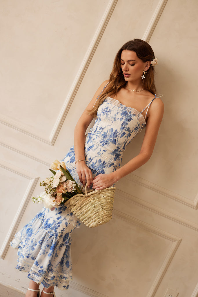 Full front view of model wearing The Geranium Dress in Provencal Blue Floral while holding a basket of flowers.